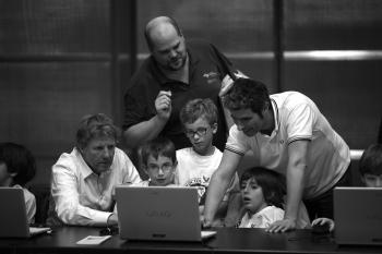 Un grup de copii cu profesorul lor în spatele unui laptop. Fotografie albă și neagră.