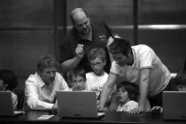 A group of kids with their teacher behind a laptop. Black and white photo.