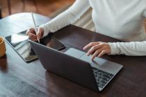 A woman typing on a laptop and taking notes on a tablet 