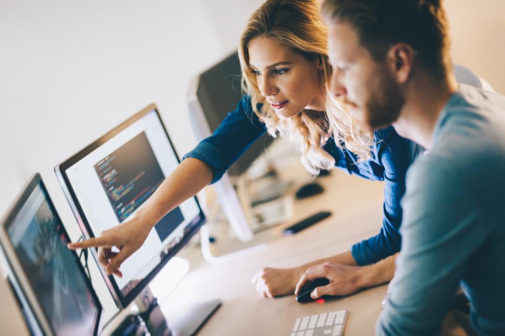 Two people working together around a desktop computer