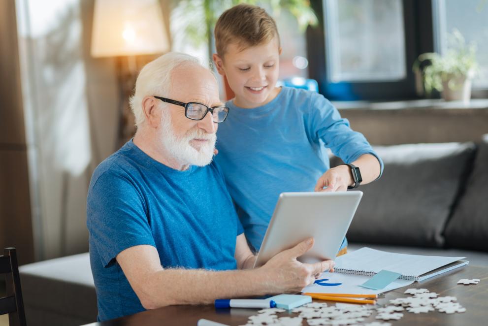 Boy standing with his grandfather andp ointing at the tablet