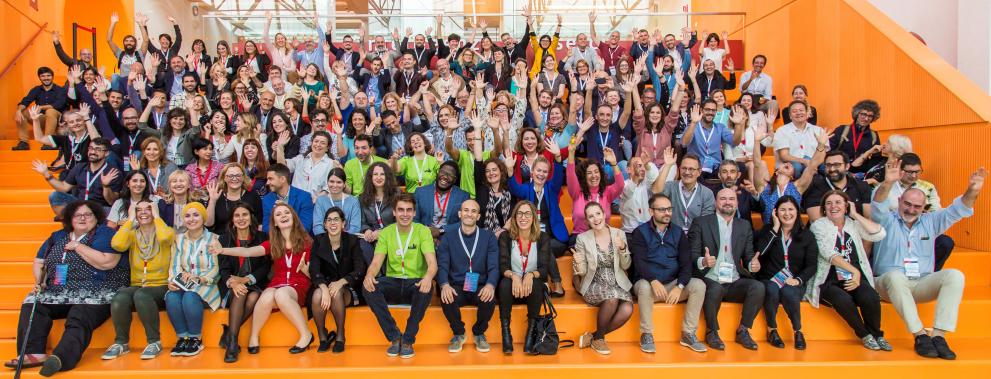 Photo of a group of people raising their arms and smiling while sitting on orange steps