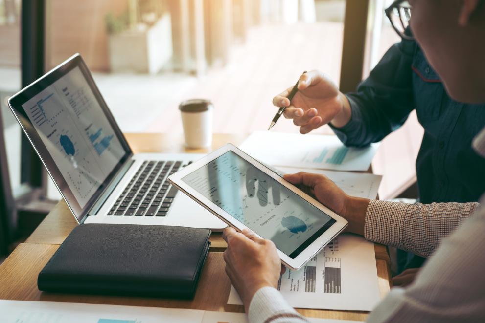 Business partnership coworkers using a tablet to chart company financial statements report and profits work progress and planning in office room. Business partnership coworkers using a tablet to chart company financial statements report and profits work progress and planning in office room.