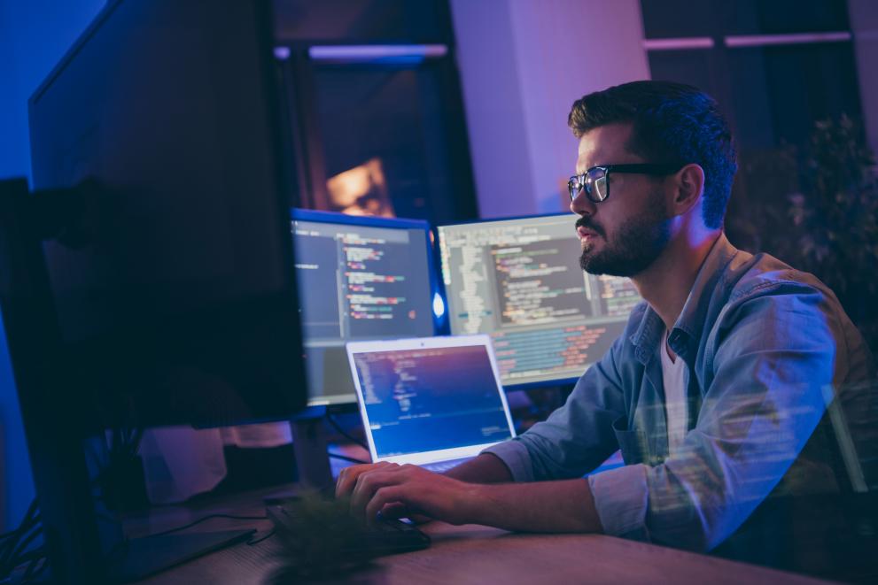 © Adobe Stock man sitting at computer screens with code
