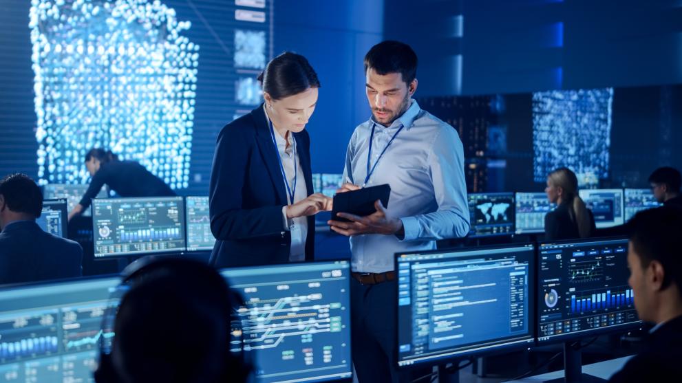 man and woman looking at a tablet in a room with computer screens