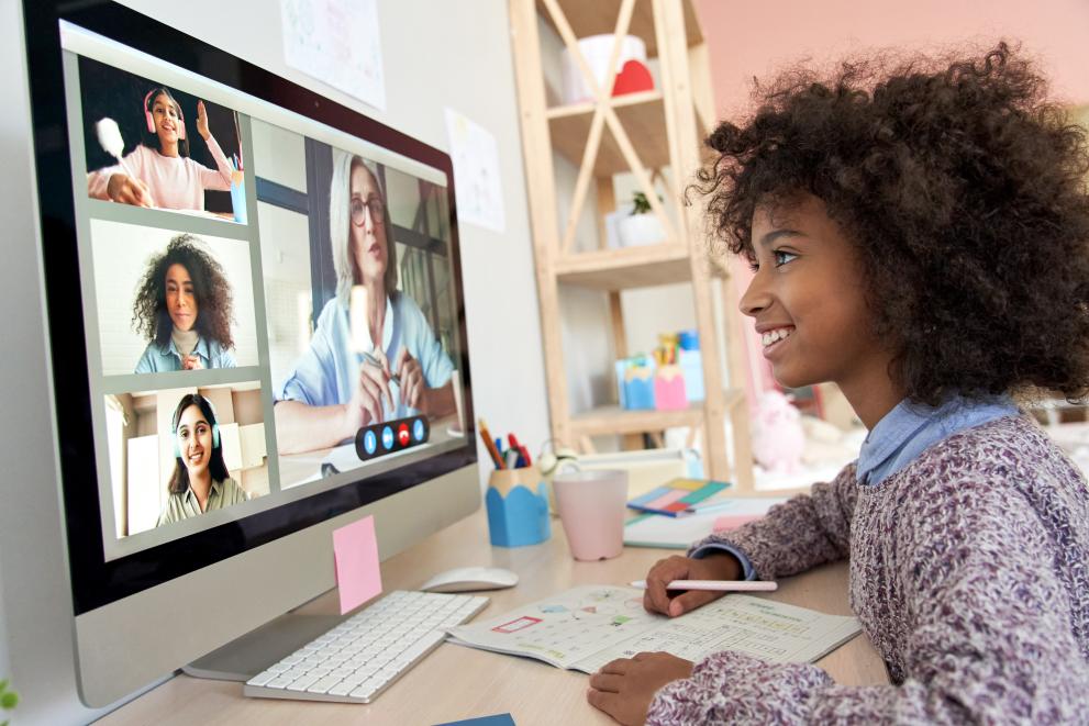© Adobe Stock a young girl with curly brown hair smiling at the screen of the computer during an online lesson
