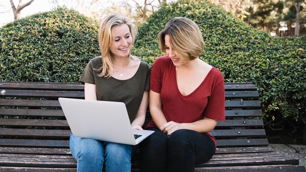 Source: freepik.com Two women sitting next to each other in front of a laptop