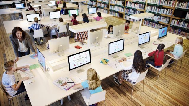 Photo of a diverse class of children around computers in a brightly lit library