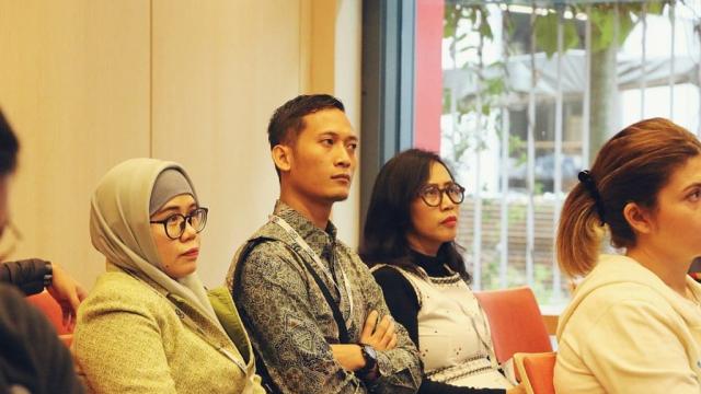 Photo of two women and a man listening in a conference hall