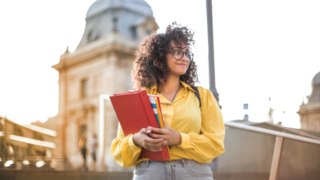 a curly brown haired girl holding a big red schoolbook