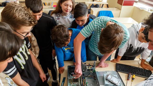 a man refurbishing a computer with students from school around him