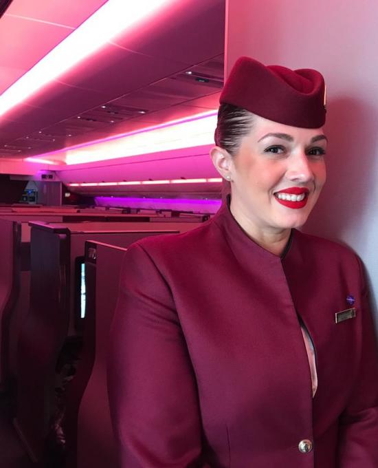 Alexia, a young woman with dark hair smiling, she is wearing a purple flight attendant uniform with a hat