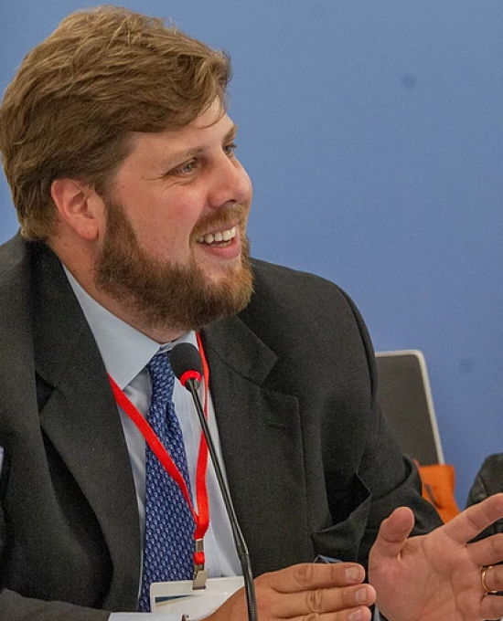 Enzo Maria Le Fevre, a man with dark blonde hair wearing a suit and a tie, speaking at a public event