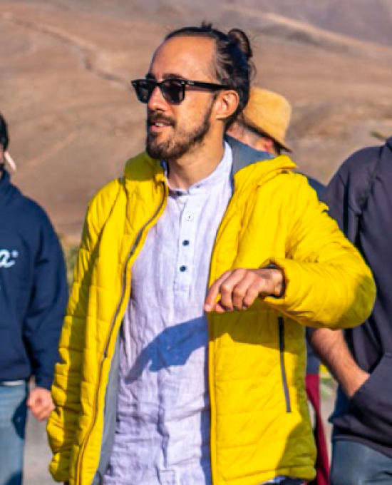 Gonzalo, a young man with dark hair tied in a bun, a yellow jacket and trekking clothes walking with other people