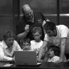 A group of kids with their teacher behind a laptop. Black and white photo.
