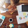 A woman on a desk working with papers, spreadsheets and a coffee around