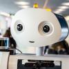 A humanoid robot sits behind a desk. 