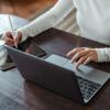 A woman typing on a laptop and taking notes on a tablet 