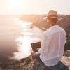 Photo of a man working on a laptop while sitting on a rock in the sunset | panophotograph
