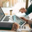 Business partnership coworkers using a tablet to chart company financial statements report and profits work progress and planning in office room. Business partnership coworkers using a tablet to chart company financial statements report and profits work progress and planning in office room.