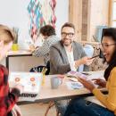 An image of three people sitting on a desk and collaborating.  An image of three people sitting on a desk and collaborating.