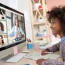 a little girl with dark skin and dark curly hair smiles at the computer screen during an online class