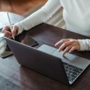 A woman typing on a laptop and taking notes on a tablet 